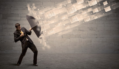 Business man protecting with umbrella against wind of papers