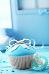 Tasty cupcake with bow and baby shoes on color wooden background
