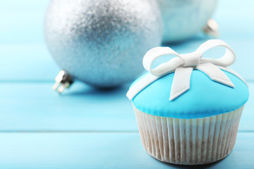 Tasty cupcake with bow and Christmas toys on color wooden background