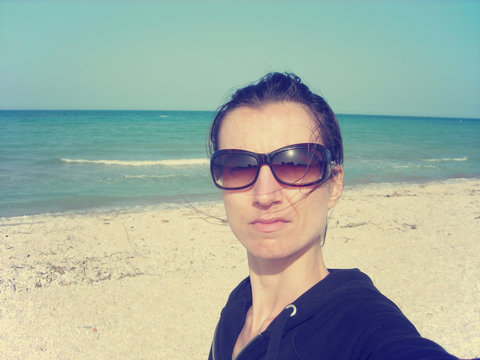 Selfie of a young woman on the beach on a sunny day, with blue sky and sea in the background. Image filtered in faded, retro, Instagram style; concept of travel and freedom.