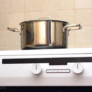 Front view of metal steel saucepan with lid on new modern glass and ceramics kitchen electric stove. Photo closeup