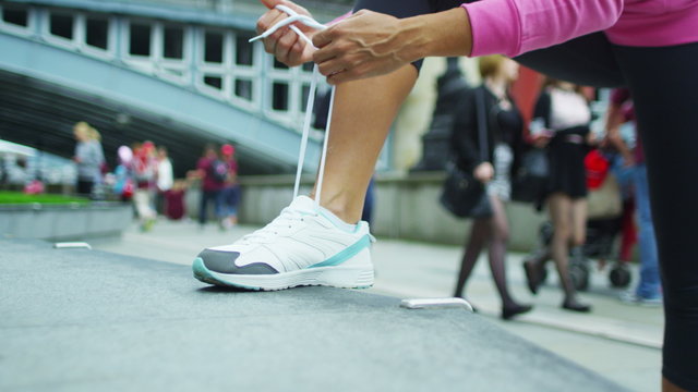  Sporty woman in urban environment ties her shoelaces in preparation to workout