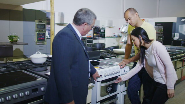 Salesman showing products to a couple in shop selling fridges and washing machines dishwashers and kitchen products. 