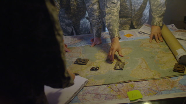  Military officers in army bunker, looking at map & discussing battle strategy
