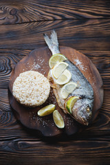 Baked dorado served with brown rice on a wooden cutting board