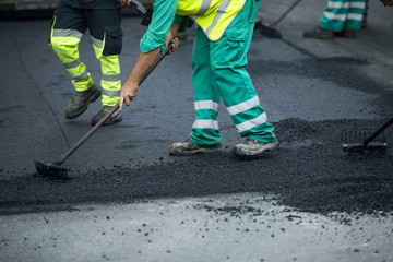 Worker operating asphalt paver machine during road construction and repairing works