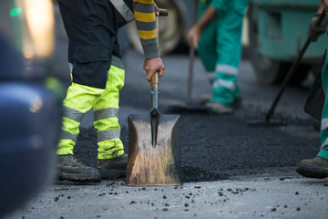 Worker operating asphalt paver machine during road construction and repairing works