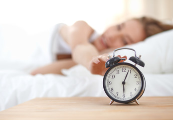 Young sleeping woman and alarm clock in bedroom at home