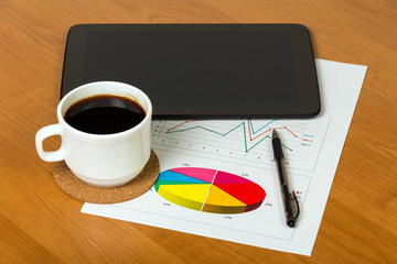 Coffee, tablet and print-out with graphs close up in the workpla