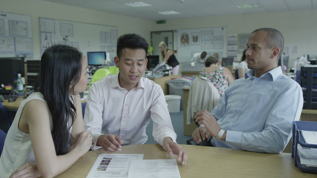 An Asian man and woman talk to black male manager in modern office building