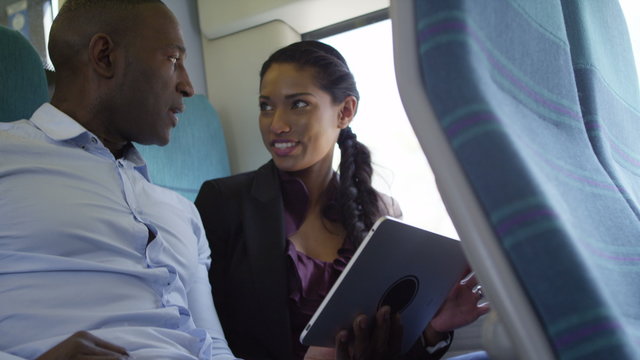  Happy attractive ethnic couple using computer tablet on train journey.