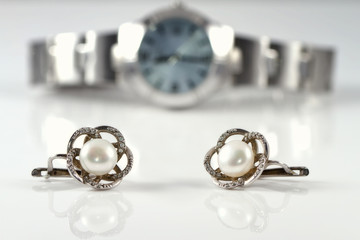 Silver earrings with pearl on the background of watches