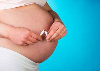 Pregnant woman breaking cigarette on blue