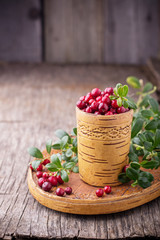 Fresh forest berries and lingonberry twigs in cup of birch bark on a wooden background.