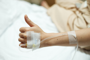 Patient hand thumbs up while given saline IV drip injection on hospital bed
