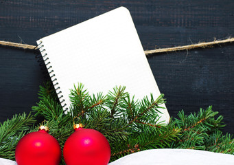 Christmas card with an empty notebook and fir-tree branches. An empty white notebook in a section for an inscription and fir tree branches on a wooden black background