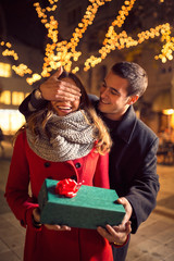romantic man standing behind woman with gift on street with Chri