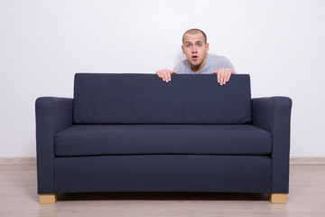 young man hiding behind a sofa