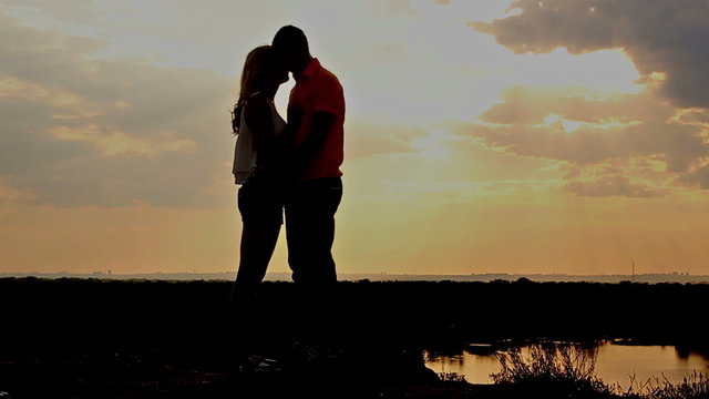 Silhouette of couple in love at sunset. A girl and a guy hug. Setting sun. A passionate kiss.