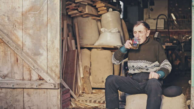 Atmospheric old grandfather in a hat sitting on a sack of flour around drinking beer barns