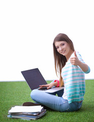 Young woman with laptop sitting on green grass