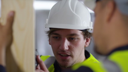  Male construction worker or tradesman working with male apprentice, showing him how to use a drill. 