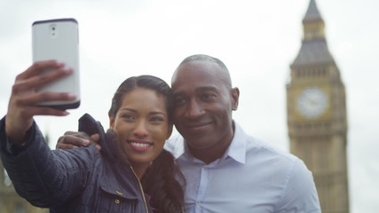 Happy attractive couple in London taking a selfie in front of houses of parliament. - Powered by Adobe