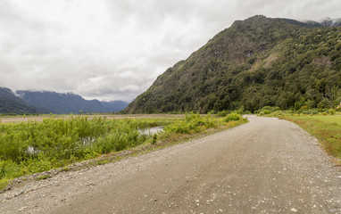 landscape photo of mountain, pond and a road with cloudy atmosphere