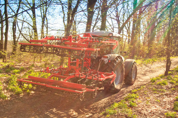 closeup cultivator on soil road against spring trees sky