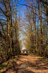 tractor on soil road in spring forest against blue sky