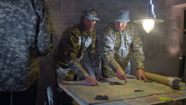  Military officers in army bunker, looking at map & discussing battle strategy