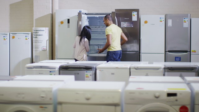 Couple shopping in a shop selling fridges and washing machines dishwashers and kitchen products. 