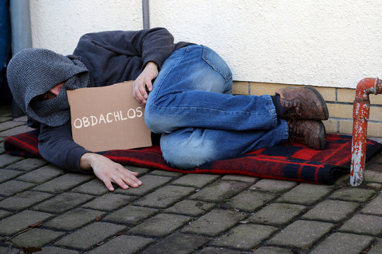 Bettler mit Schild "Obdachlos"