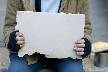 Homeless man holding a cardboard sign. - obrazy, fototapety, plakaty