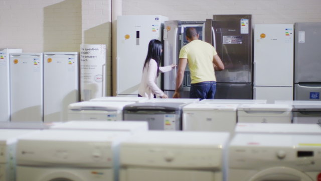 Couple shopping in a shop selling fridges and washing machines dishwashers and kitchen products. 