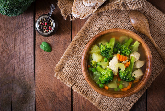 Chicken soup with broccoli, green peas, carrots and celery in  bowl on a wooden background in rustic style. Top view