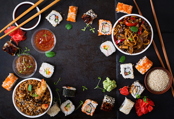 Traditional Japanese food - sushi, rolls, rice with shrimp and udon noodles with chicken and mushrooms on a dark background. Top view