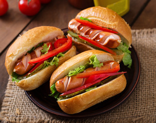 Hot dog - sandwich with pickles, paprika and lettuce on wooden background
