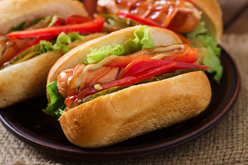 Hot dog - sandwich with pickles, paprika and lettuce on wooden background