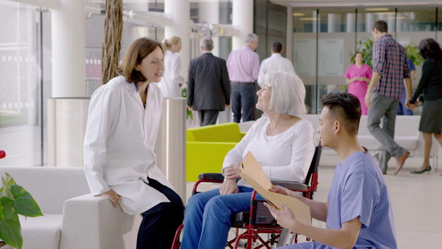  Caring medical staff talking to patient in wheelchair in busy modern hospital