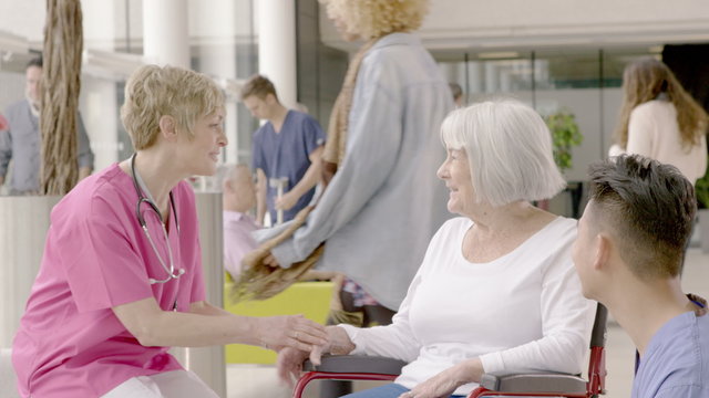  Caring medical staff assisting patient in wheelchair in busy modern hospital