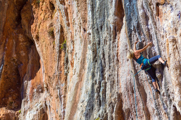 Blond Female Climber ascending Vertical Orange Rock