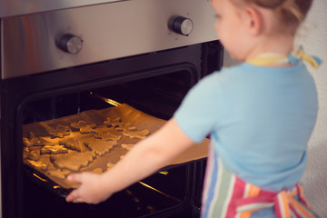 Cute little girl baking Christmas cookies in oven