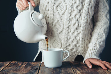 Woman in warm sweater pours tea from teapot to cup