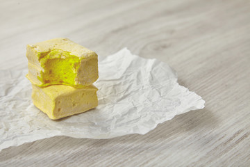 Two yellow marshmallows in column on craft paper. One bite