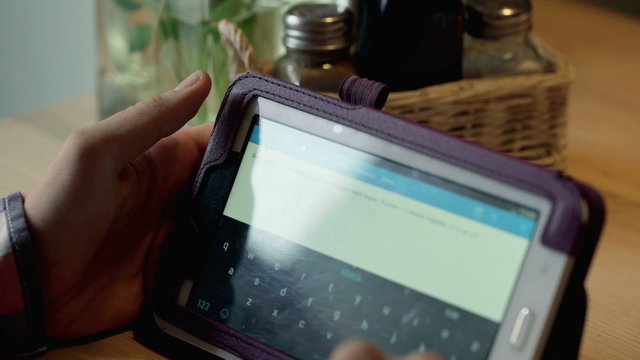 Boy sitting at the table and typing on tablet in the cafe
