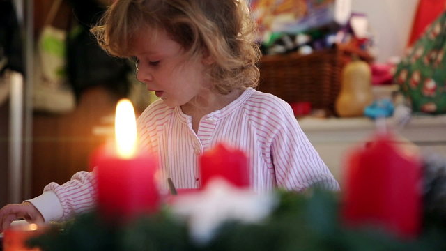 Playing with the focus on a burning candle with a little girl sorting out cookies in the background on advent first