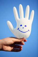 hand holding smiling glove against blue sky.