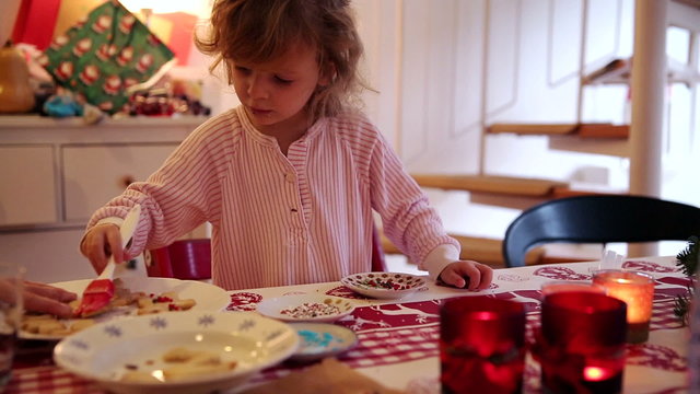 A little girl puts icing on some cookies while her mother is holding them tight on advent first