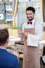 Cheerful young waiter is serving a customer